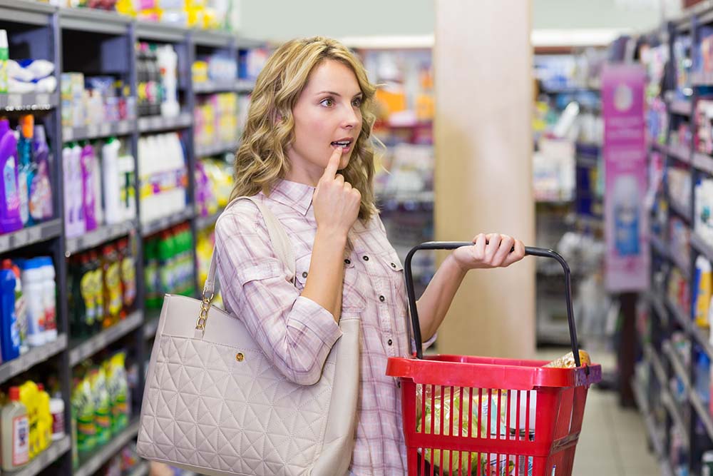 Woman with shopping bag looking thoughtfully at supermarket shelf