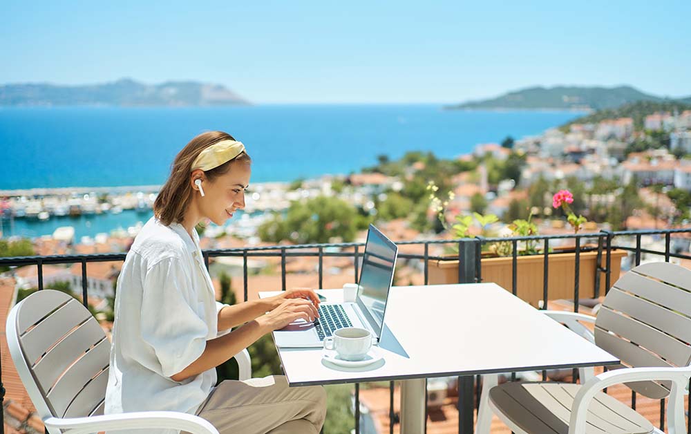 Remote working while evaluating Bulgarian living comfort Woman working remotely on laptop from scenic terrace overlooking Bulgarian coastal city assessing living comfort