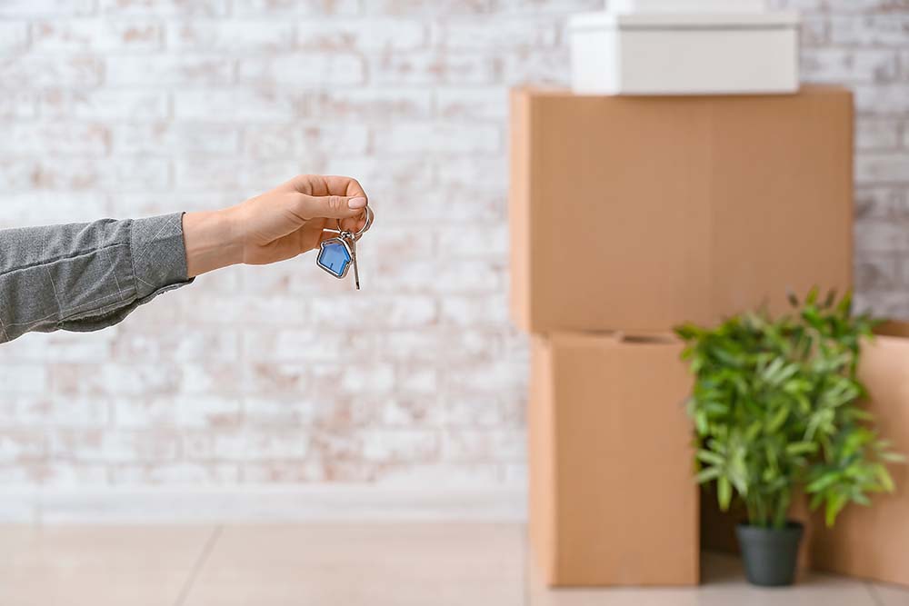 Understanding rental income taxation for residents Hand holding keys with moving boxes representing rental income taxation for residents and non-residents