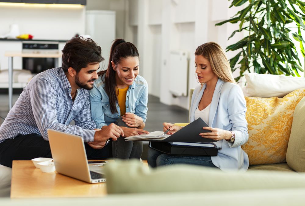 Three people sit with a laptop and documents, discussing market analysis and property prices in Bulgaria