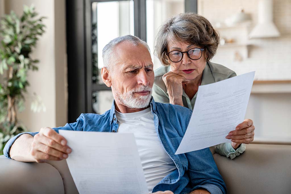 An elderly couple sits on a sofa, carefully studying financial and legal documents concerning property issues in Bulgaria