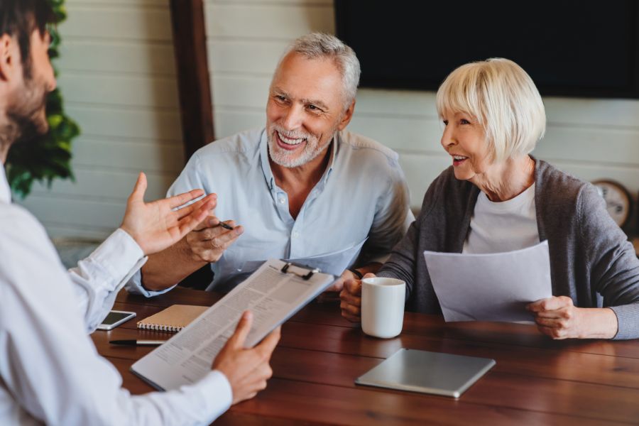 A happy elderly couple discusses documents concerning pension and moving to Bulgaria with a consultant.